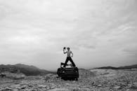 Unrecognizable man with naked torso standing on abandoned car in suburbs