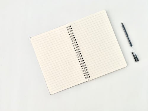 Spiral notepad with lines near pen on white background