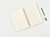 Spiral notepad with lines near pen on white background