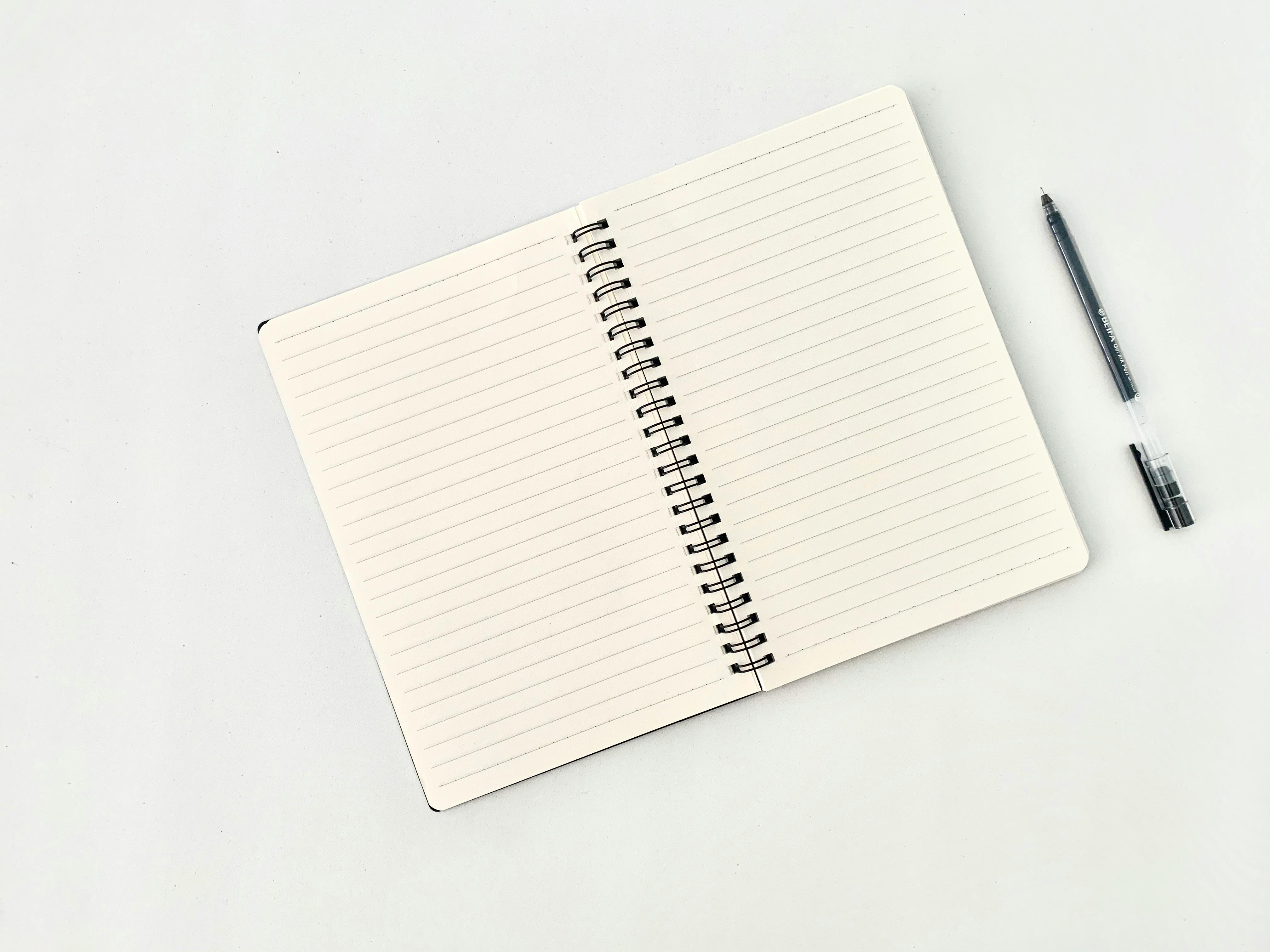 Spiral notepad with lines near pen on white background \u00b7 Free Stock Photo