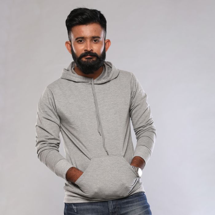 Man in a heather grey pullover hoodie standing against a soft grey studio backdrop — photo by Lappen Fashion on Pexels