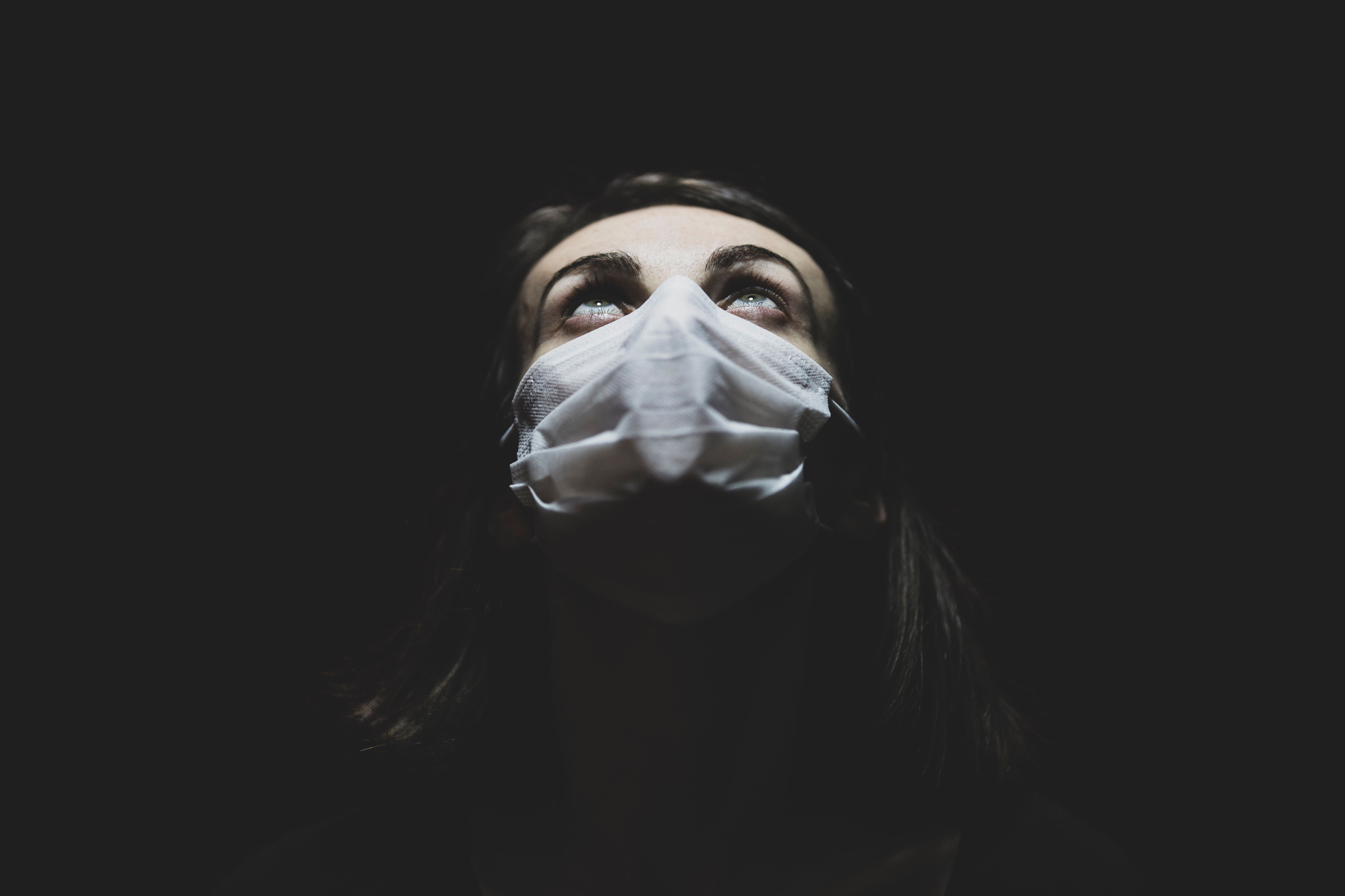 在黑暗的环境中，一名戴着口罩的女子抬头仰望，象征着大流行时代