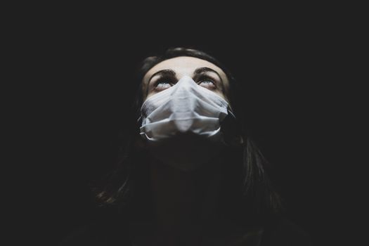 在黑暗的环境中，一名戴着口罩的女子抬头仰望，象征着大流行时代