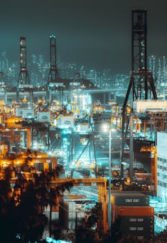Dynamic nighttime aerial view of Hong Kong's bustling shipping port with illuminated cranes and containers.