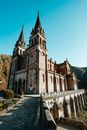 From below of aged stone Catholic Basilica de Santa Maria la Real de Covadonga with sharp roofs and ornamental details located in Spain against cloudless blue sky