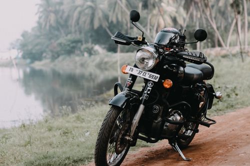 Free Classic Royal Enfield motorcycle parked on a dirt road beside a serene lake with lush greenery. Stock Photo
