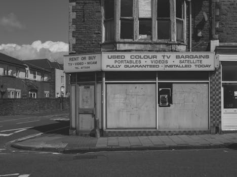 Black and white of old abandoned building with vintage shop of used electronic goods on empty street of city