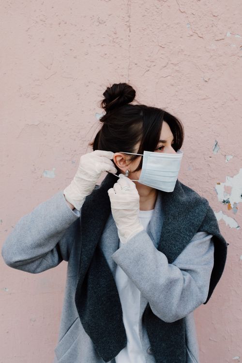 Free Adult woman in gloves adjusting protective mask against a pink wall. Stock Photo