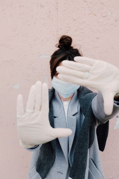 Free Woman in face mask and gloves posing against a pink wall, highlighting safety and fashion. Stock Photo