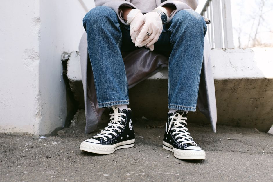 Person sitting outdoors wearing jeans, sneakers, and gloves. Urban street fashion captured.