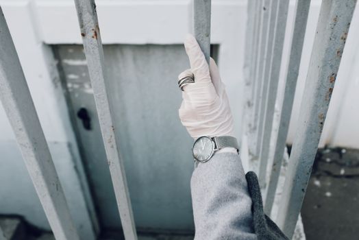 A gloved hand wearing a watch and ring holds onto a metal fence outdoors, symbolizing protection.