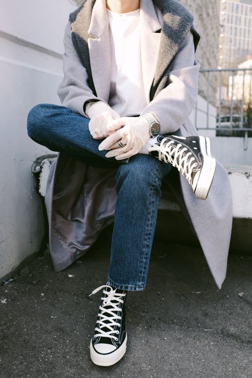 Free Person sitting outdoors wearing stylish sneakers and latex gloves, a gray coat, and jeans. Stock Photo