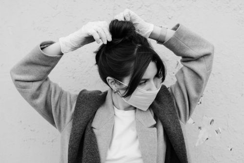 Free Grayscale image of a woman wearing a face mask and gloves adjusting her hair. Stock Photo