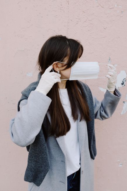 A woman wearing gloves adjusts her face mask outdoors, reflecting pandemic precautions.