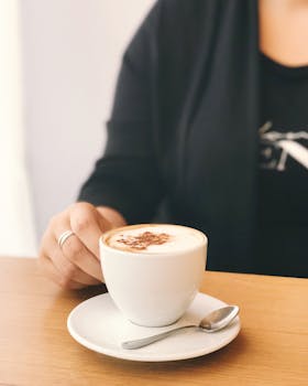 特写：一位端着卡布奇诺的女人在室内木桌旁