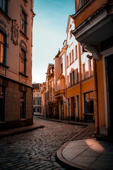 Empty narrow cobblestone street between aged buildings against blue sky on sunny day