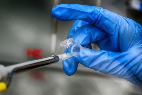 Crop unrecognizable scientist in blue latex gloves taking sample from plastic tube in modern laboratory