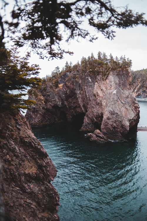 Free Huge rocky formation in ocean surrounded by cliffs and trees against overcast sky in Canada Stock Photo