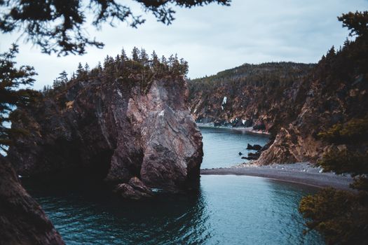 Amazing scenery of massive cliff formation with coniferous trees growing on top above lake harbor