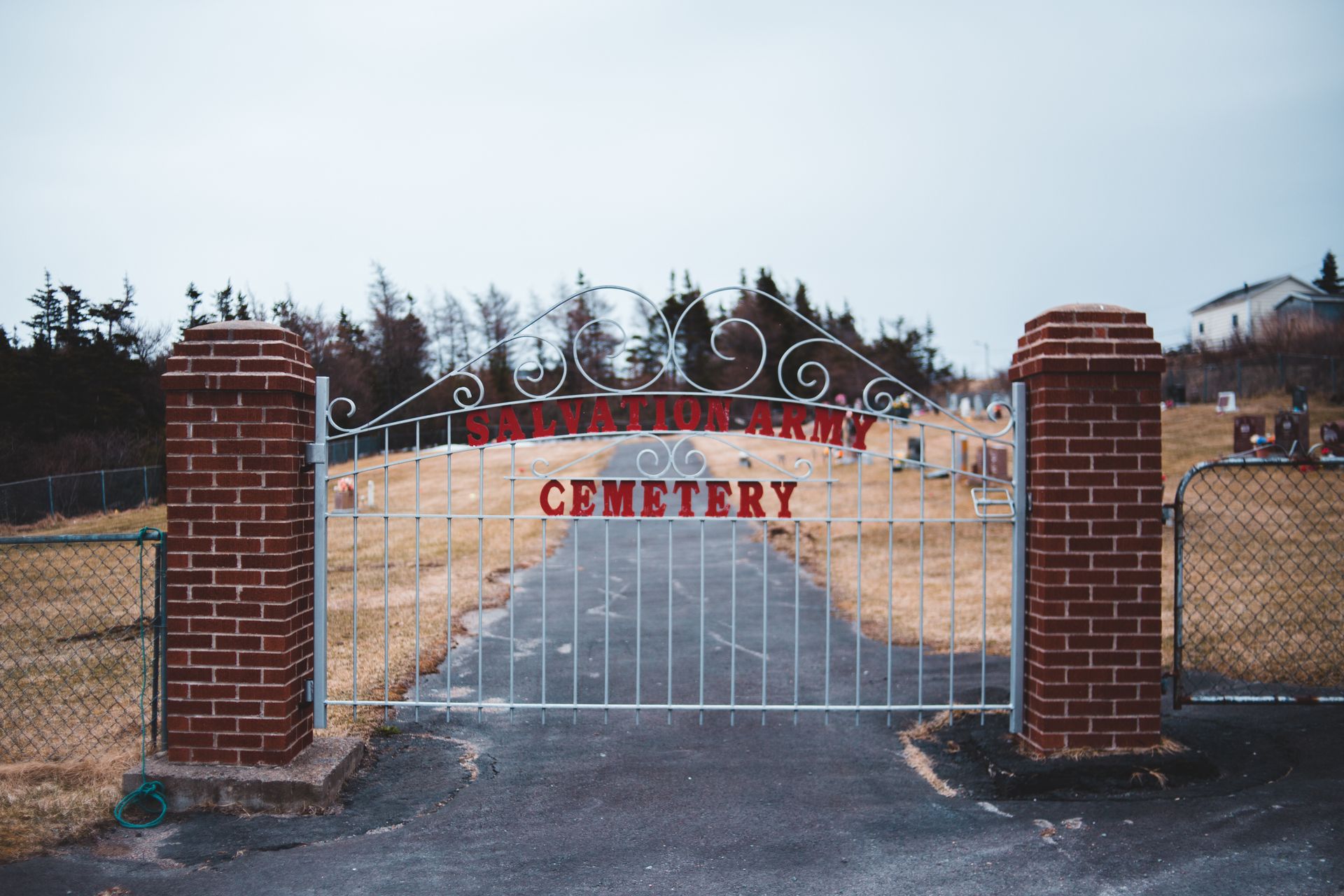 Countryside road and closed entrance to army cemetery with metal bars on gloomy day