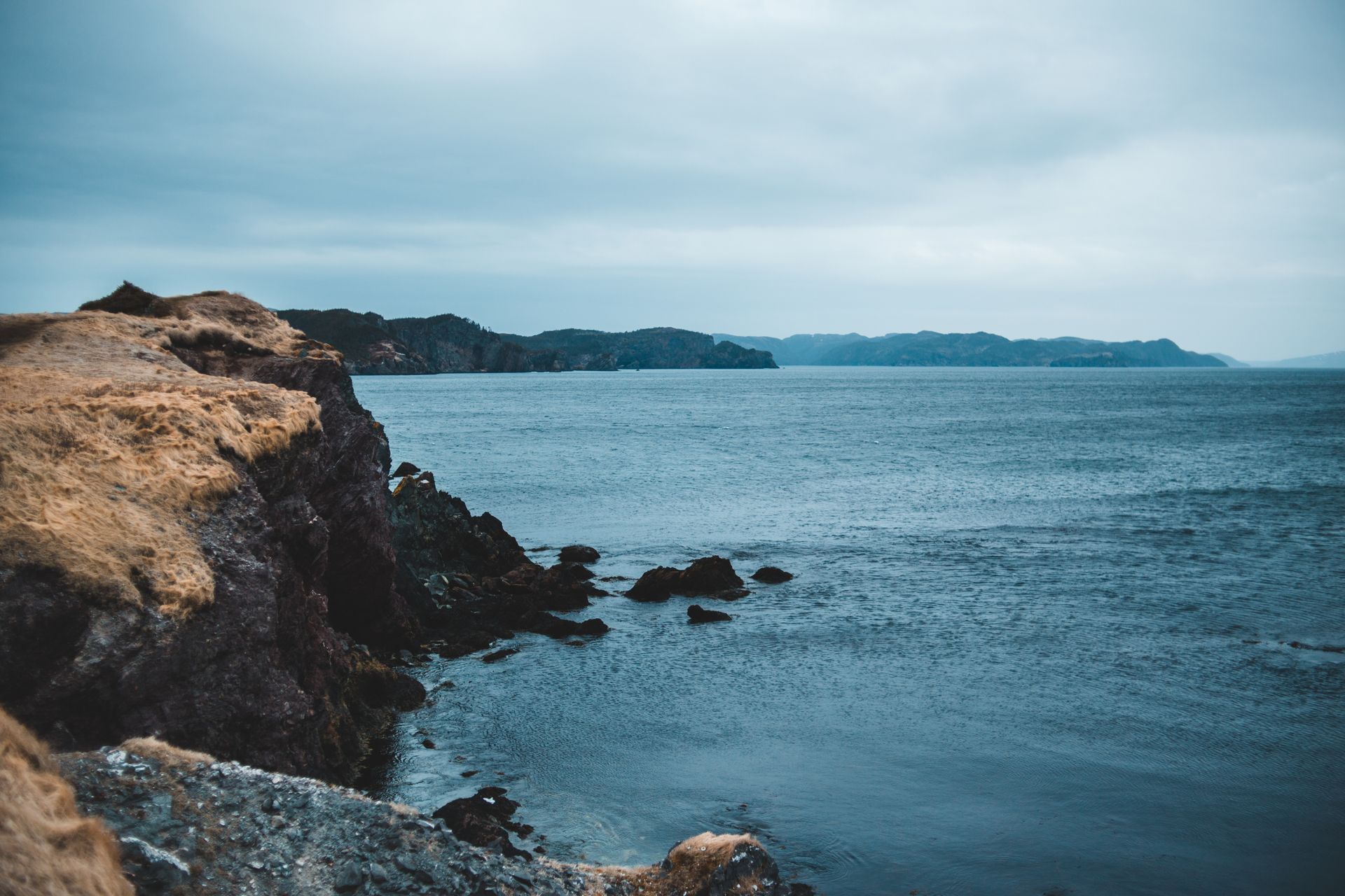 High angle of rough stony coast with steep slopes near calm sea and mountains on horizon