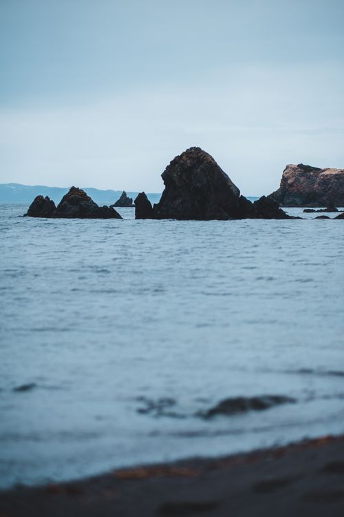 Free Rough stony cliff in calm sea with rippling water against overcast gray sky Stock Photo