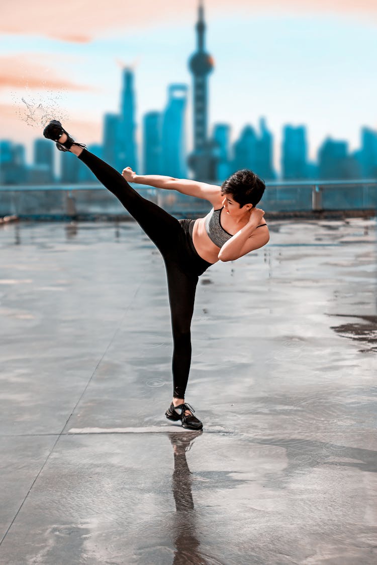 A Woman In Gray Tank Top And Black Leggings In Kicking Position