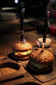 Close-up view of gourmet hamburgers with knives on wooden boards, emphasizing their delicious, freshly made appearance.