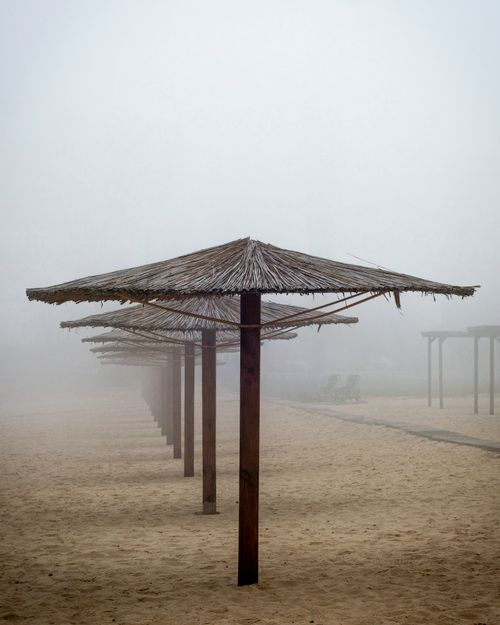 Free Misty beach scene with wooden nipa hut umbrellas in fog, creating a tranquil atmosphere. Stock Photo
