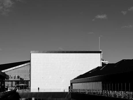 一张极简主义的黑白照片中，一座现代建筑和一个孤独的人物，共同营造出荒凉的城市场景