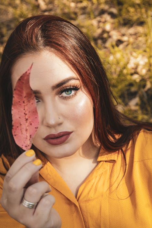 Young woman with bright makeup covering face with leaf