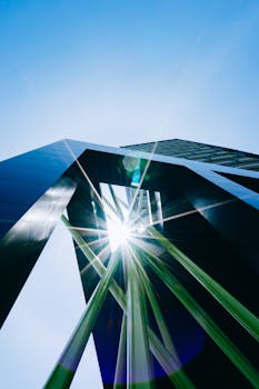 从低角度仰望现代摩天大楼，其抽象设计在晴朗蓝天的映衬下，与朝阳相映成趣