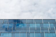 当代玻璃建筑正面呈现出几何图案，并反射着多云的天空