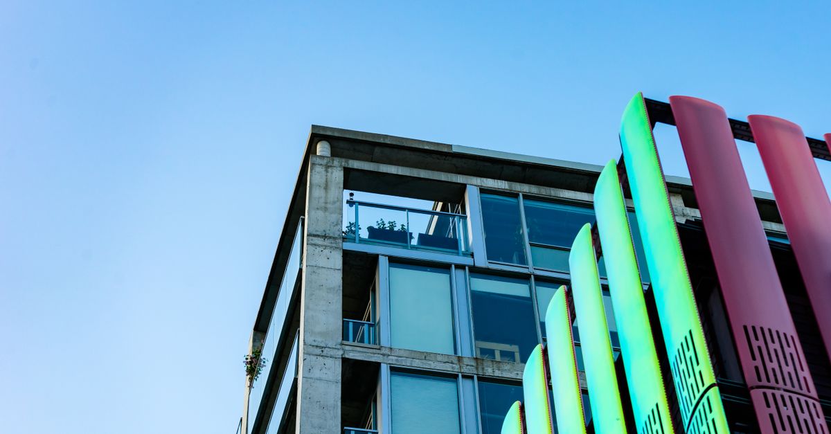 Low angle view of a modern building facade with vibrant glass panels against a clear sky.