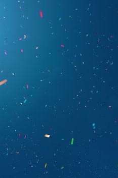 Abstract background of festive bright multicolored confetti falling down against blue water surface