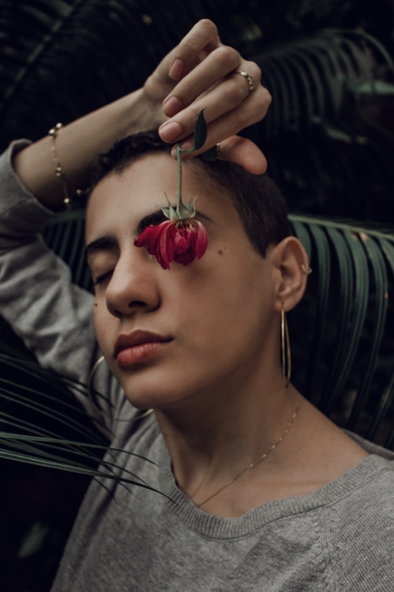 Close-up of a woman holding a vibrant red flower against lush green tropical leaves in Santarém, Brazil.