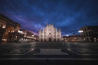 Low angle of aged masonry church exterior near square and buildings under bright sky in evening in Italy