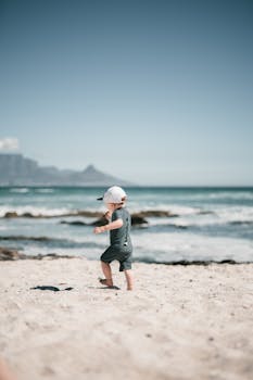 一个小男孩在沙滩上奔跑，晴朗的蓝天下，背景是海浪
