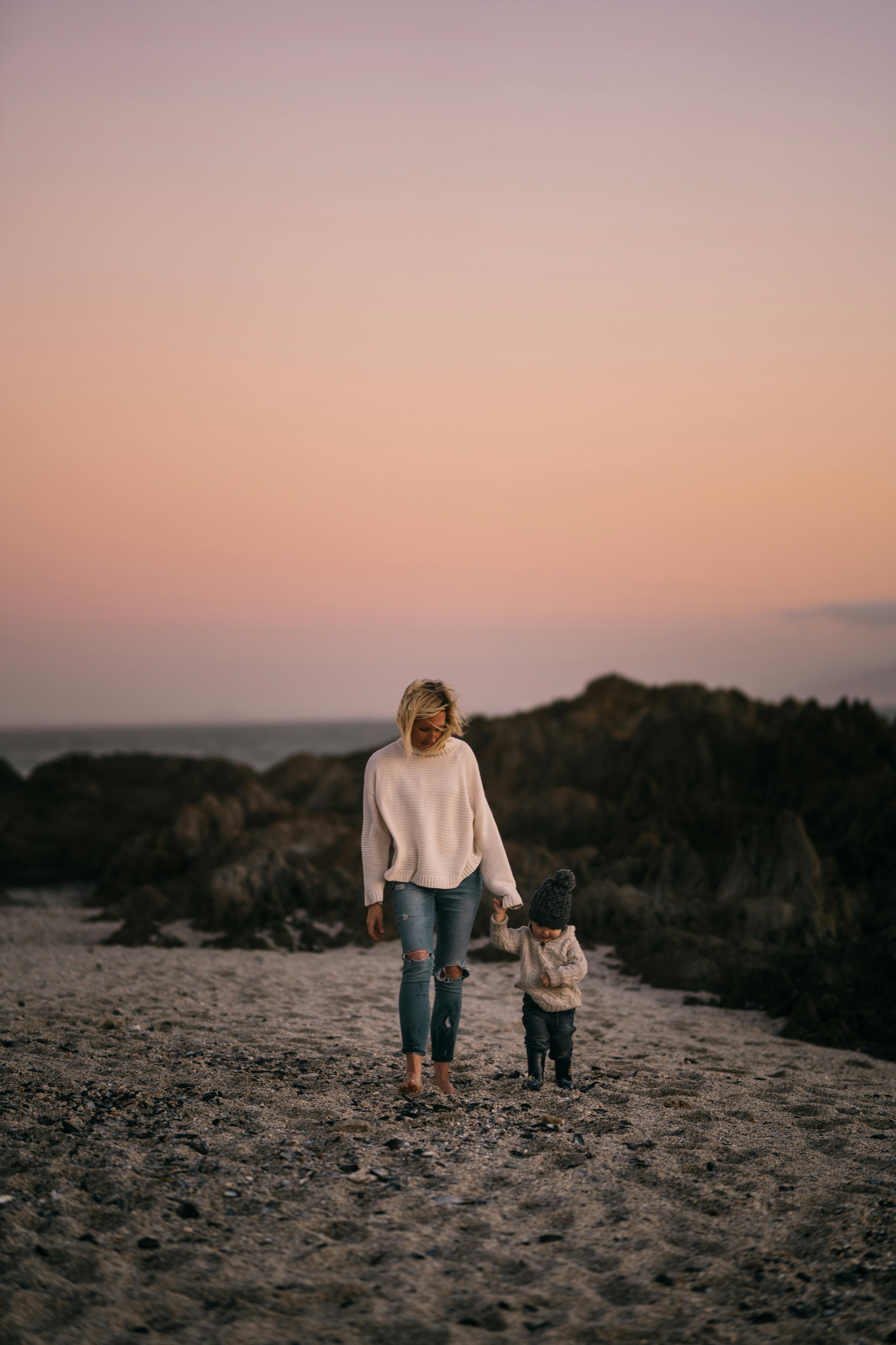 日落时分，母亲和孩子手牵着手在海滩上散步，营造出温暖的家庭时光