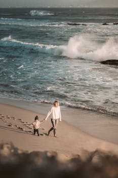一对母子沿着海滩散步，背景是汹涌的海浪，捕捉到了一个宁静的家庭时刻