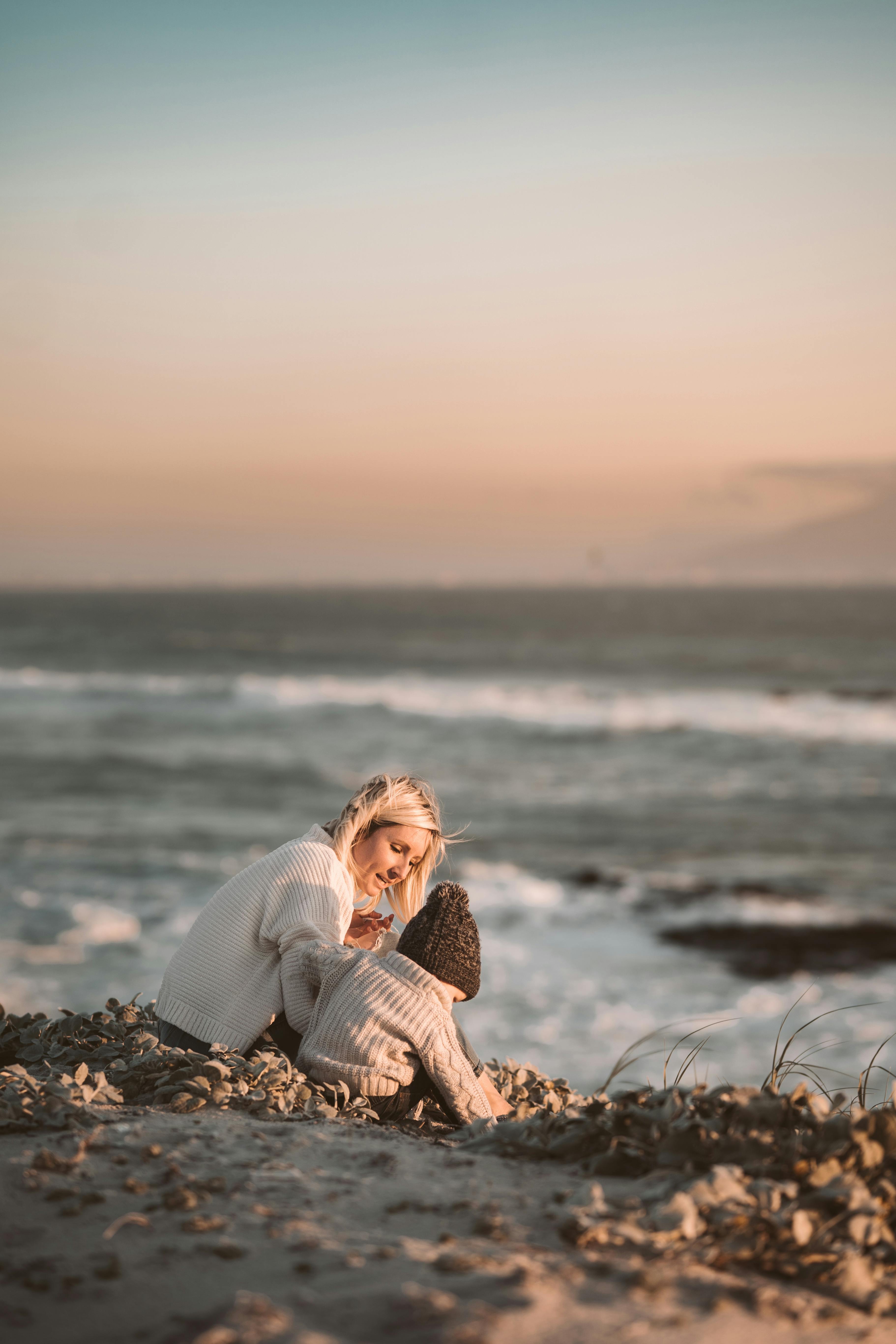 a woman and her child sitting on the shore