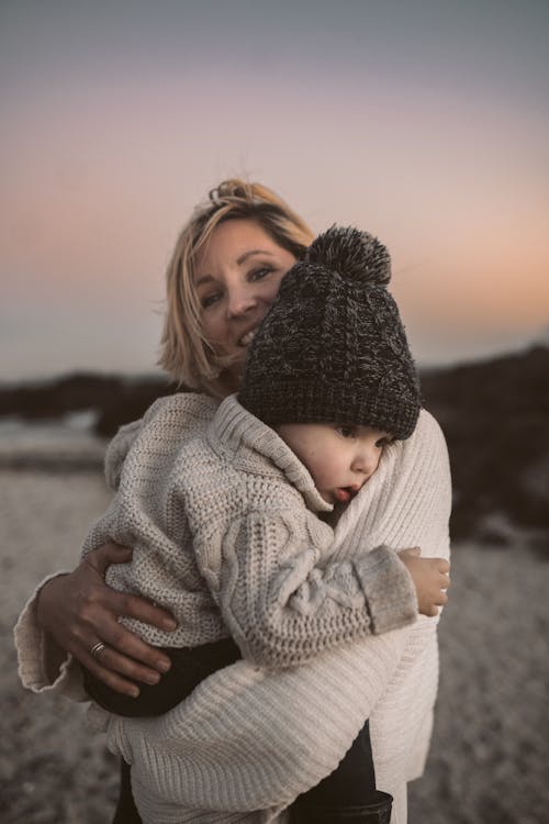 Photo of a Woman Carrying Her Baby in Knitted Clothes