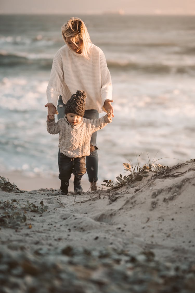 A Woman And Her Child Walking On The Sand