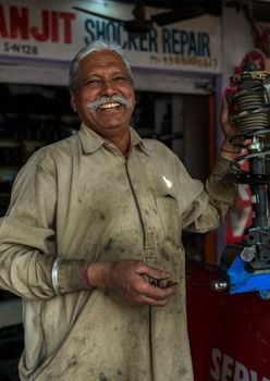 Cheerful elderly ethnic male worker in dirty uniform standing near equipment and looking at camera in workroom
