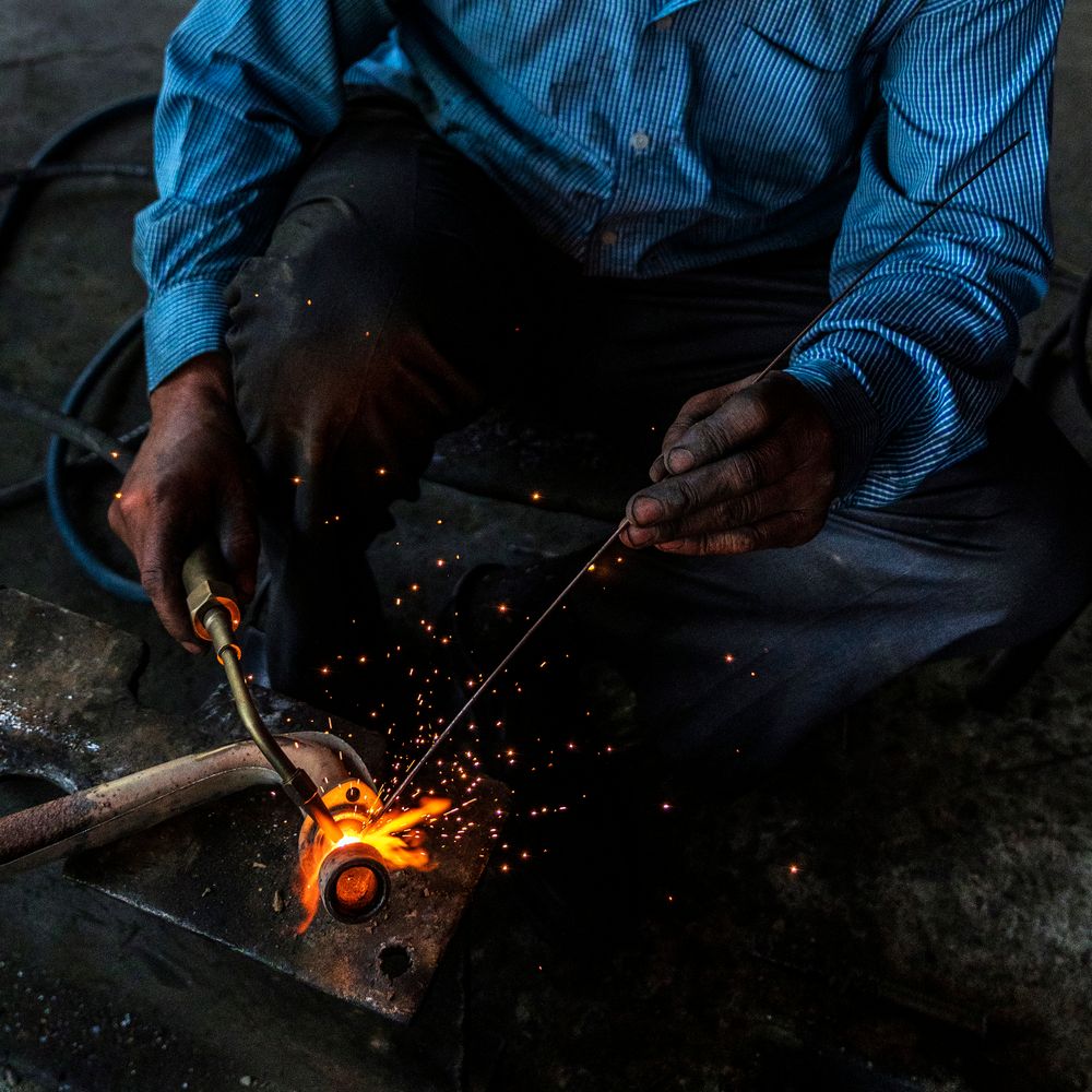 Welder running a root pass on a steel pipe at ground level.