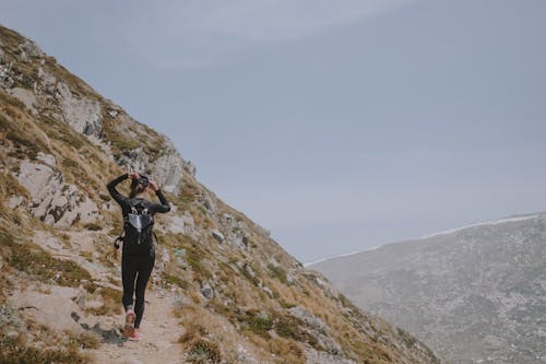 Woman in Black Long Sleeve Shirt and Black Pants Standing on Rocky Mountain