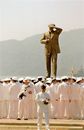 Aged stone statue of military male near unrecognizable army in white uniform behind green mountain