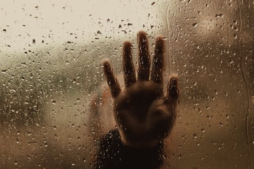 Hand of unrecognizable person behind wet window