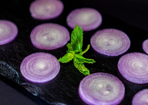 Close-up of vivid purple onion slices with fresh green mint leaves on a black surface.