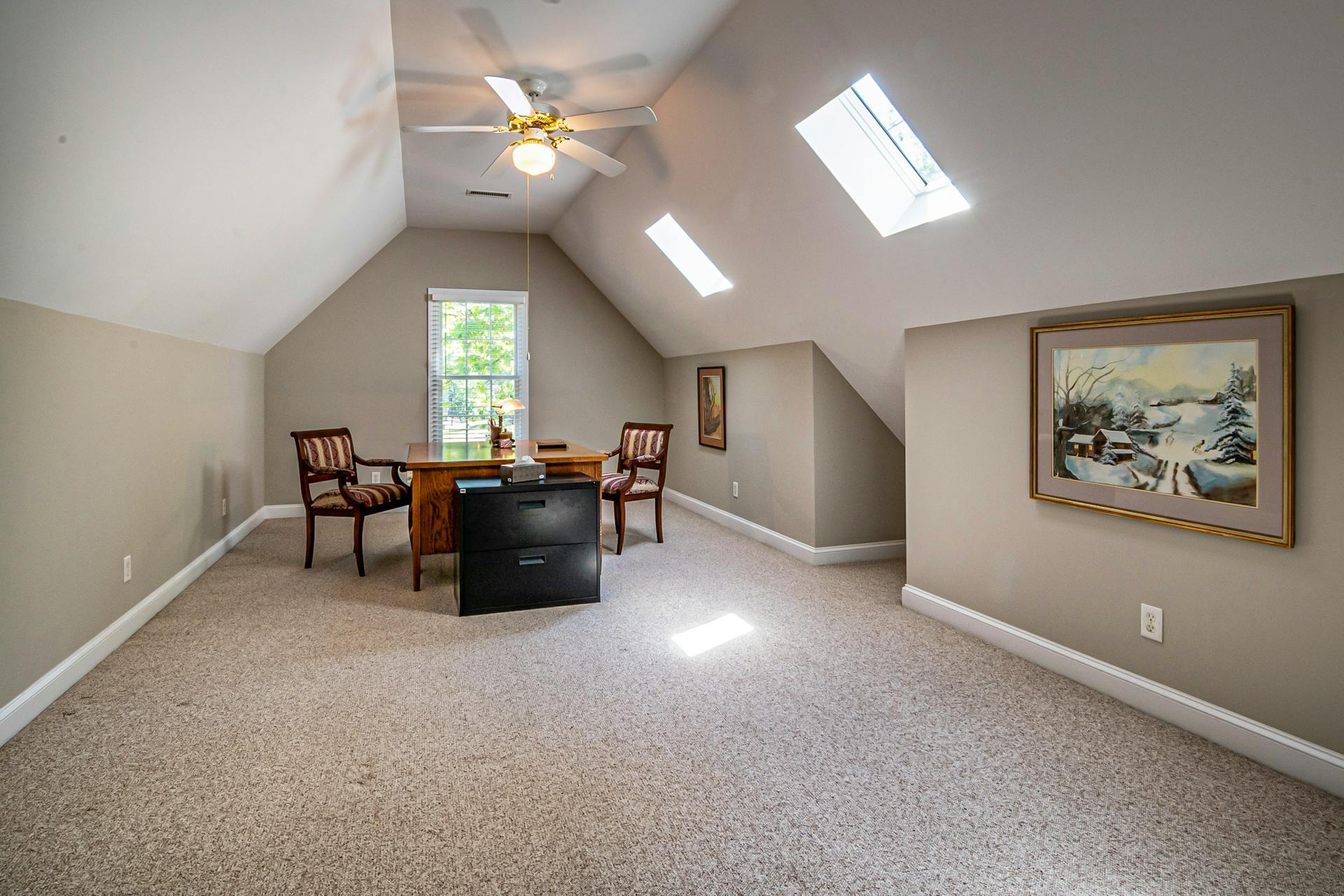 Bright attic home office featuring a desk, chairs, and natural lighting from skylights.